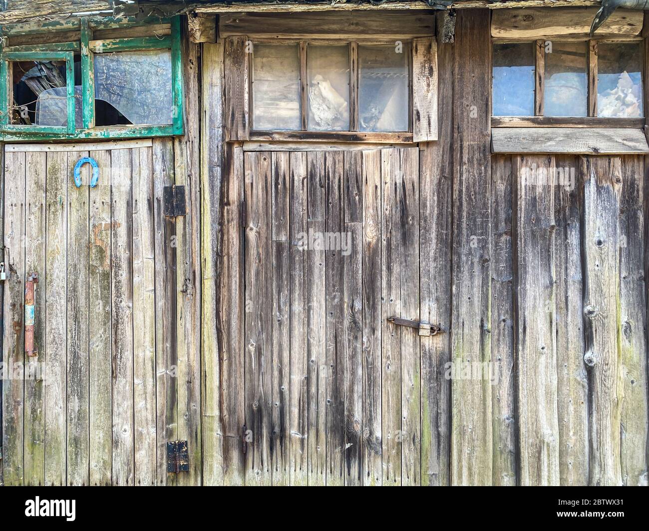 Alte verwitterte hölzerne Scheunenwand. Geschlossene Türen mit Vorhängeschlössern und Fenster mit Glasbruch Stockfoto