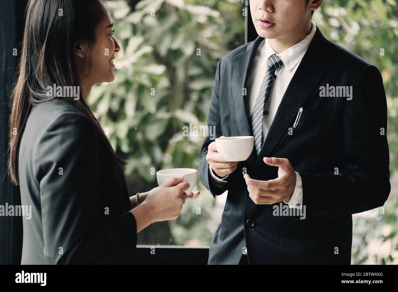 Kaffeepause. Gruppe Geschäftsleute, stehen in modernen Büro, halten eine Tasse, lächelnd stehen am Fenster Stockfoto