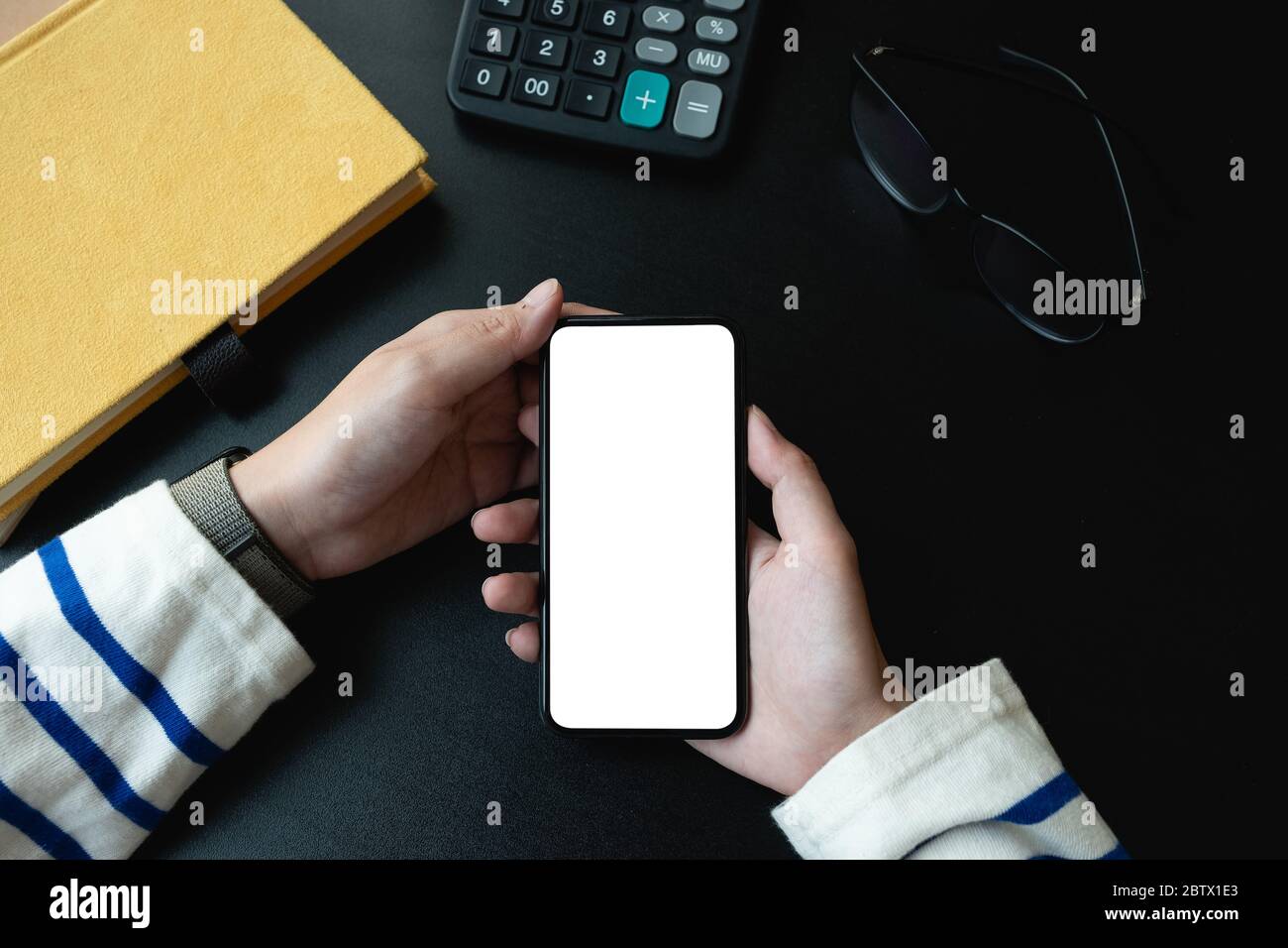 Draufsicht der Frau mit leerem Bildschirm Smartphone in dunklen trendigen Arbeitsplatz Stockfoto