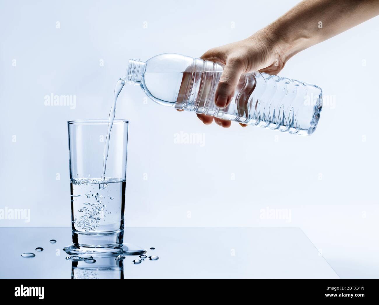 Hand gießen frisches reines Wasser aus der Flasche in ein Glas auf dem Tisch mit Wassertropfen, Gesundheits-und Beauty-Hydratation-Konzept Stockfoto