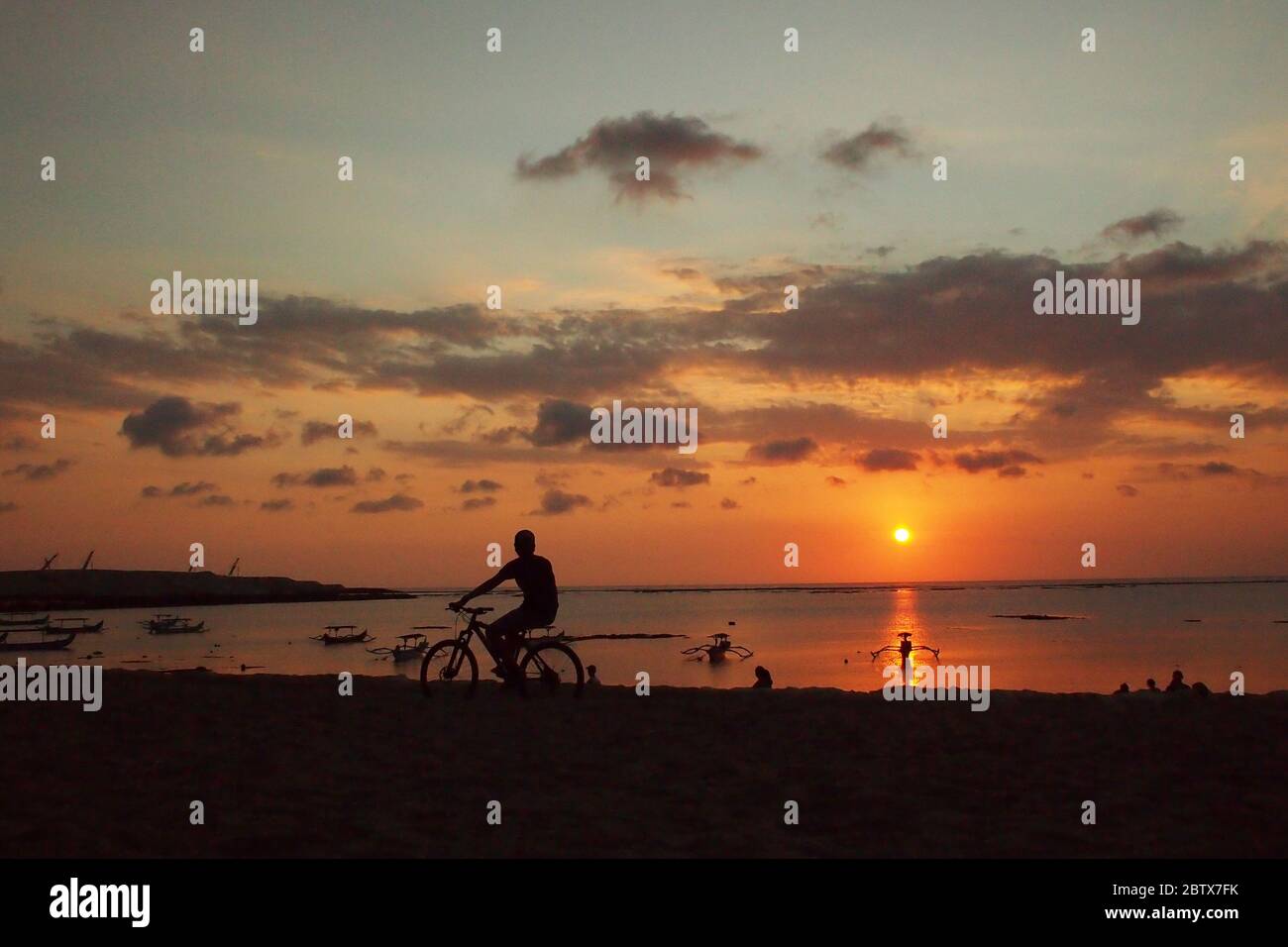Silhouette eines Touristen auf einem Fahrrad, der den Sonnenuntergang mit einer dramatischen Atmosphäre des Himmels beobachtet Stockfoto