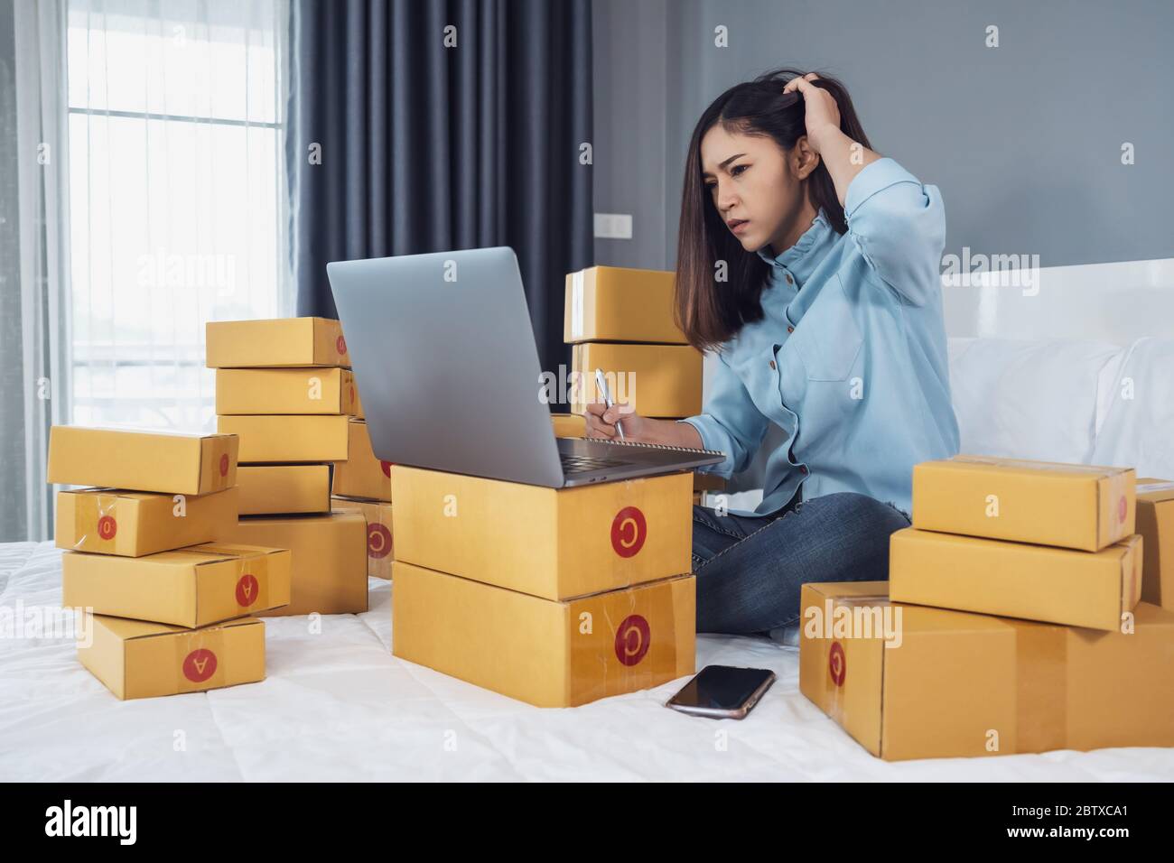 Gestresste Frau mit Laptop-Computer und Arbeits Problem, um Produkt online auf einem Bett zu Hause zu verkaufen Stockfoto