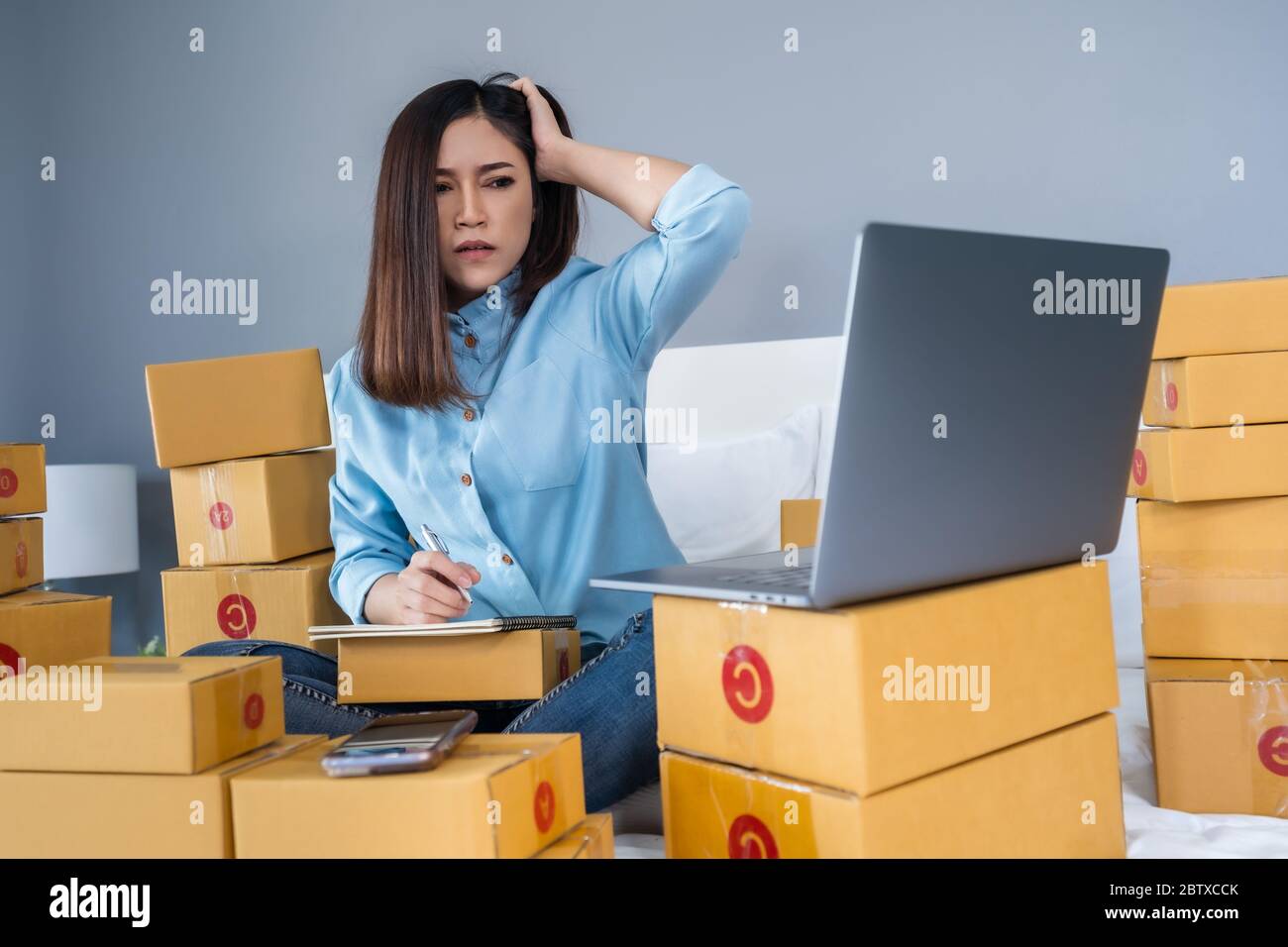 Gestresste Frau mit Laptop-Computer und Arbeits Problem, um Produkt online auf einem Bett zu Hause zu verkaufen Stockfoto