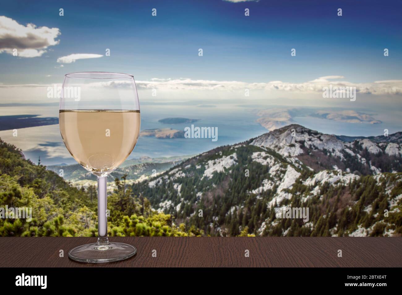 Glas Weißwein mit Blick auf die Berge und das Meer und blauer Himmel mit Wolken in Kroatien Stockfoto