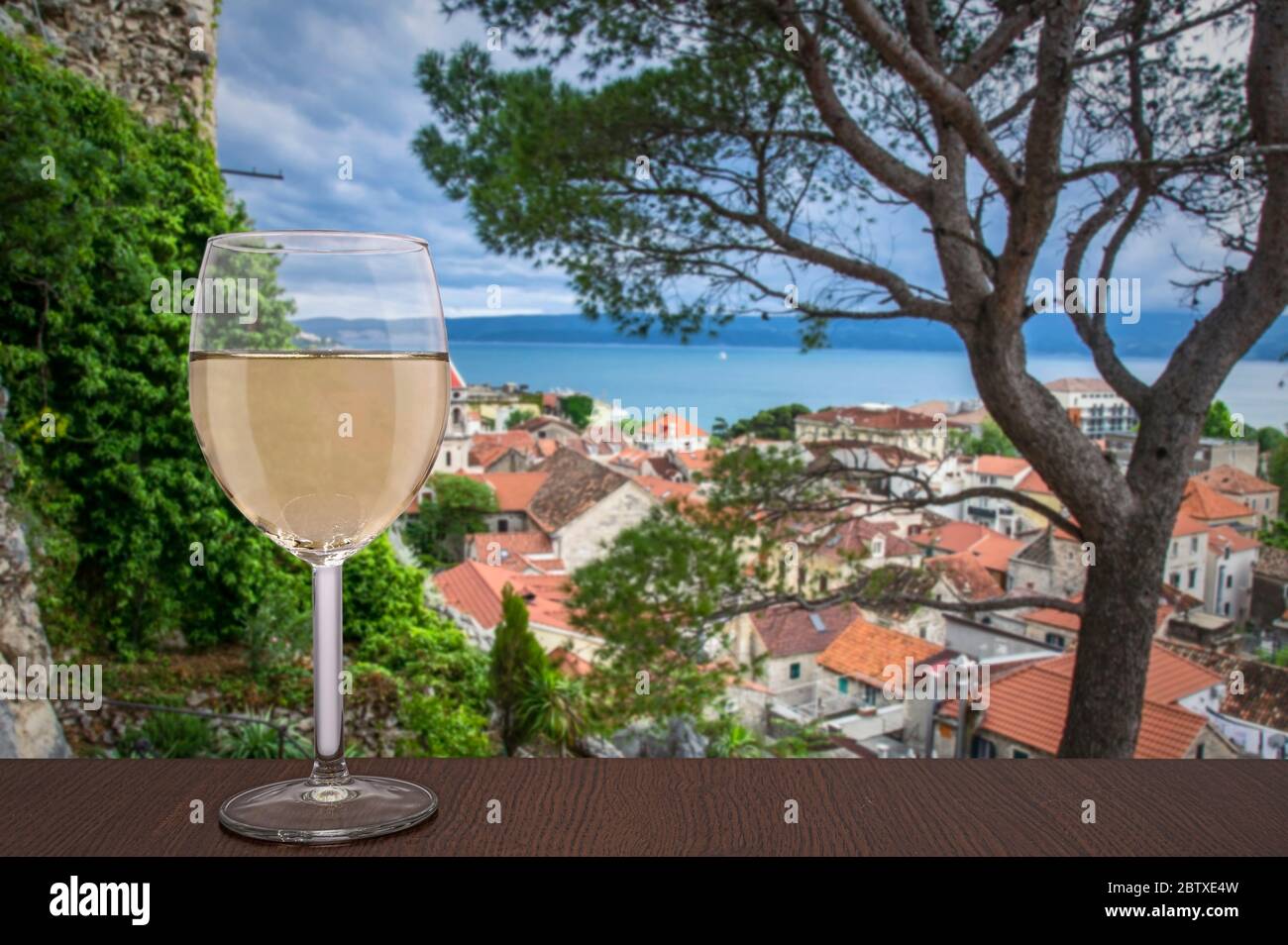 Glas Wein auf Meer verschwimmen Hintergrund und alte mediterrane Stadt Omis in Kroatien. Rote Dächer der historischen Altstadt. Stockfoto