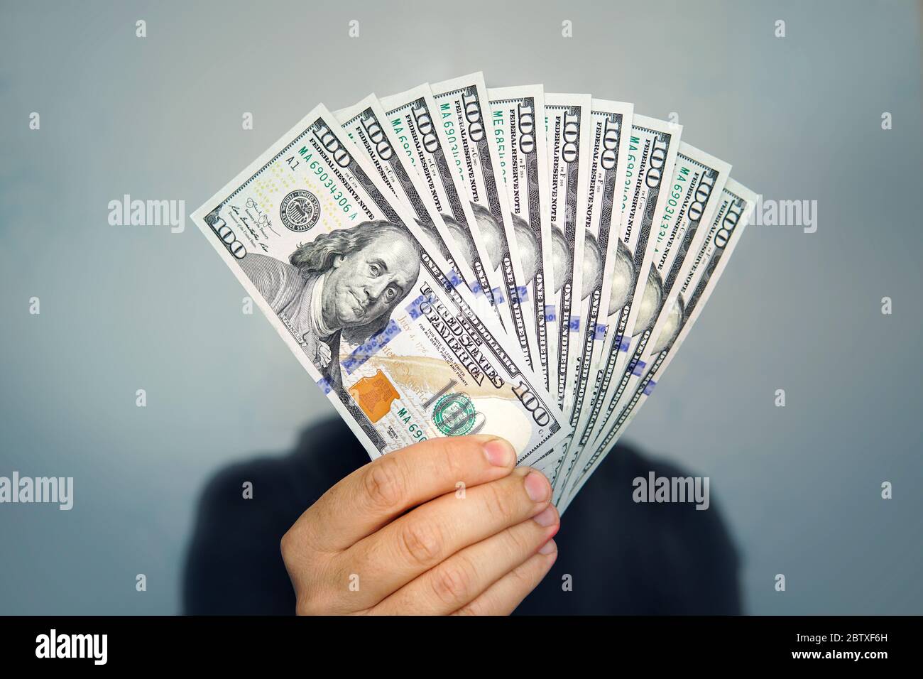 1000 Dollar in 100 Scheinen in der Hand eines Mannes Nahaufnahme auf einem dunklen Hintergrund. Hände, die Bargeld in Dollar halten Stockfoto