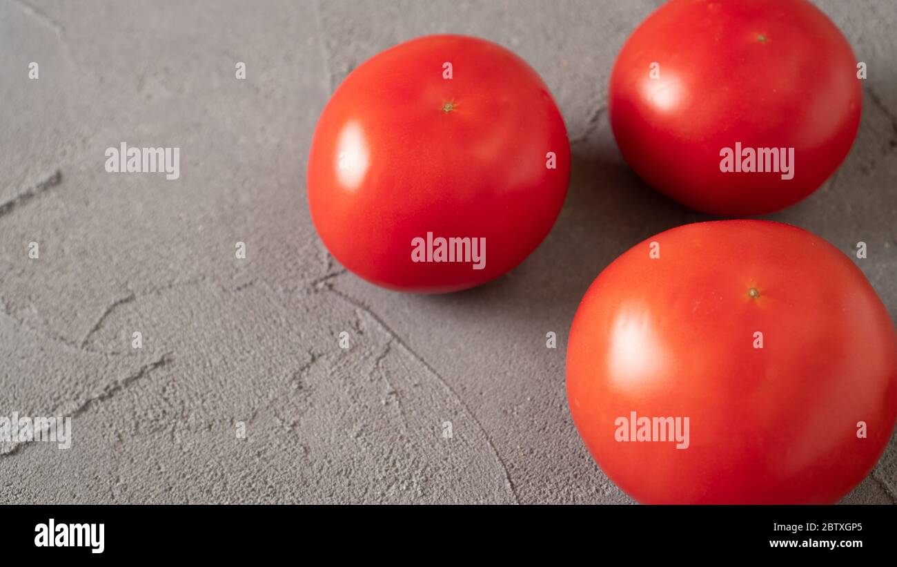 Drei frische Tomaten auf einem Betontisch. Ein Bündel Tomaten auf einem grauen Hintergrund. Reife rote Tomaten. Draufsicht Stockfoto