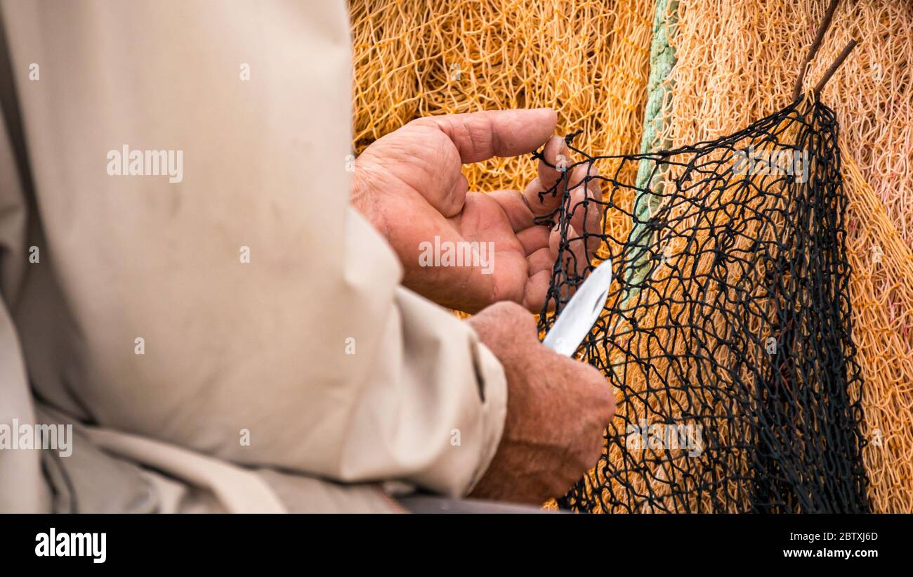Nahaufnahme des Fischers, der das Fischernetz mit dem Messer repariert. Stockfoto