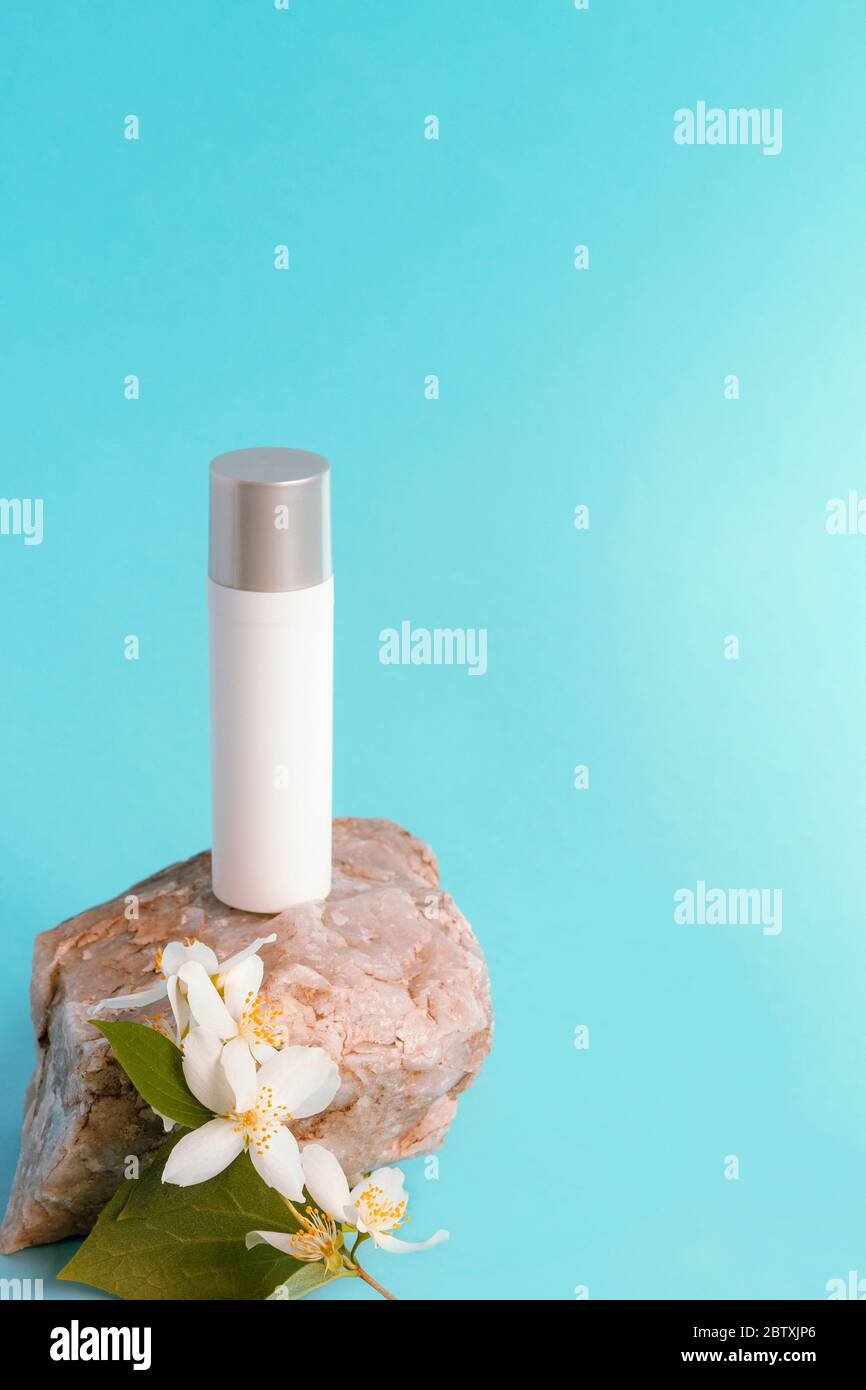 Kosmetische Serum-Flasche in weiß blank Paket auf dem Stein mit Jasminblüte, blauer Hintergrund, Kopierer Raum. Selektiver Fokus Stockfoto