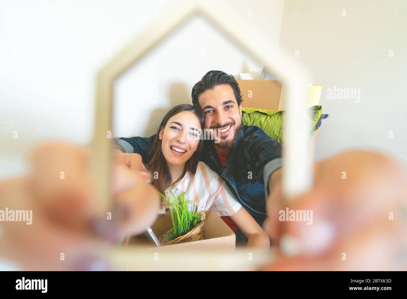 Glückliches junges Paar, das zum ersten Mal nach Hause zieht - Mann und Frau haben Spaß beim Auspacken der Kartonschachtel im neuen Haus Stockfoto