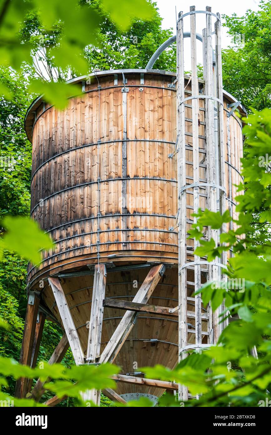 Der hölzerne Wassertank auf dem Hintergrund von grünen Bäumen. Der Tank ist  auf einer Holzstruktur mit Rohren und einer Leiter angebracht  Stockfotografie - Alamy