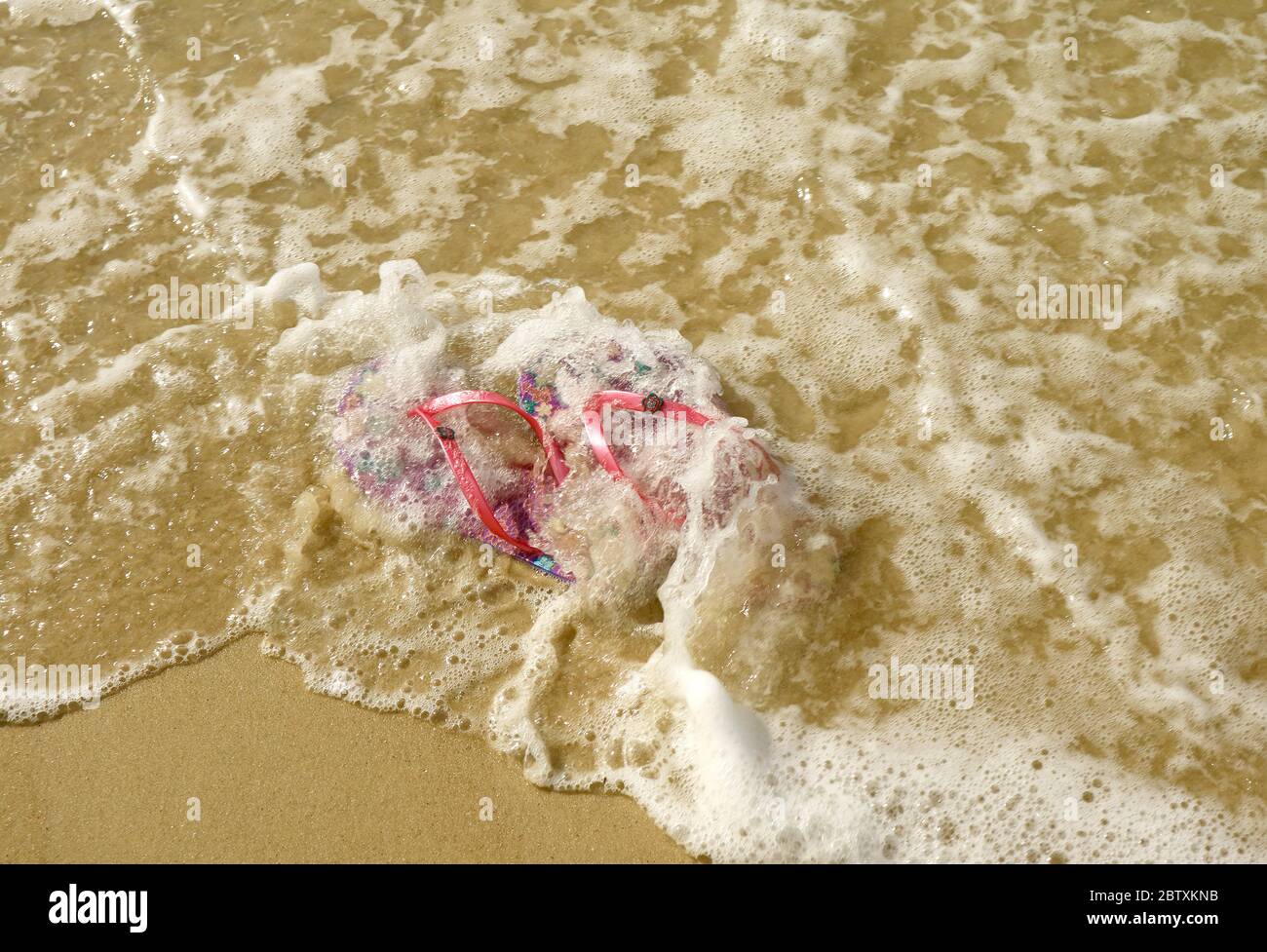 Ein Paar leuchtend rosa Flip-Flops Sandalen am Strand, die von den Wellen des Meeres krachen Stockfoto