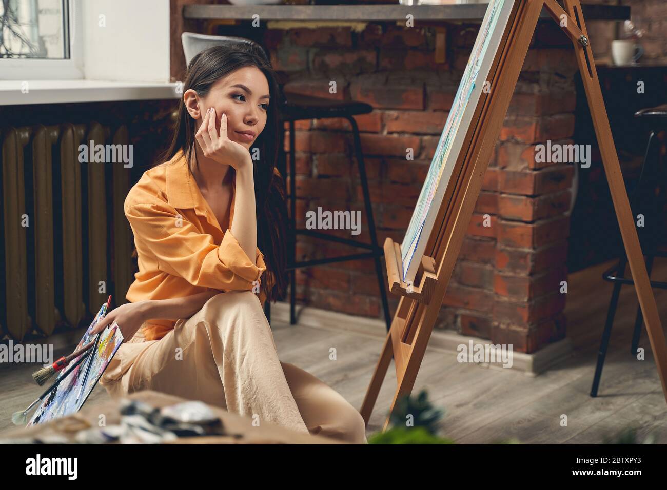 Attraktive Dame, die ihr Gemälde im Heimkunststudio ansieht Stockfoto