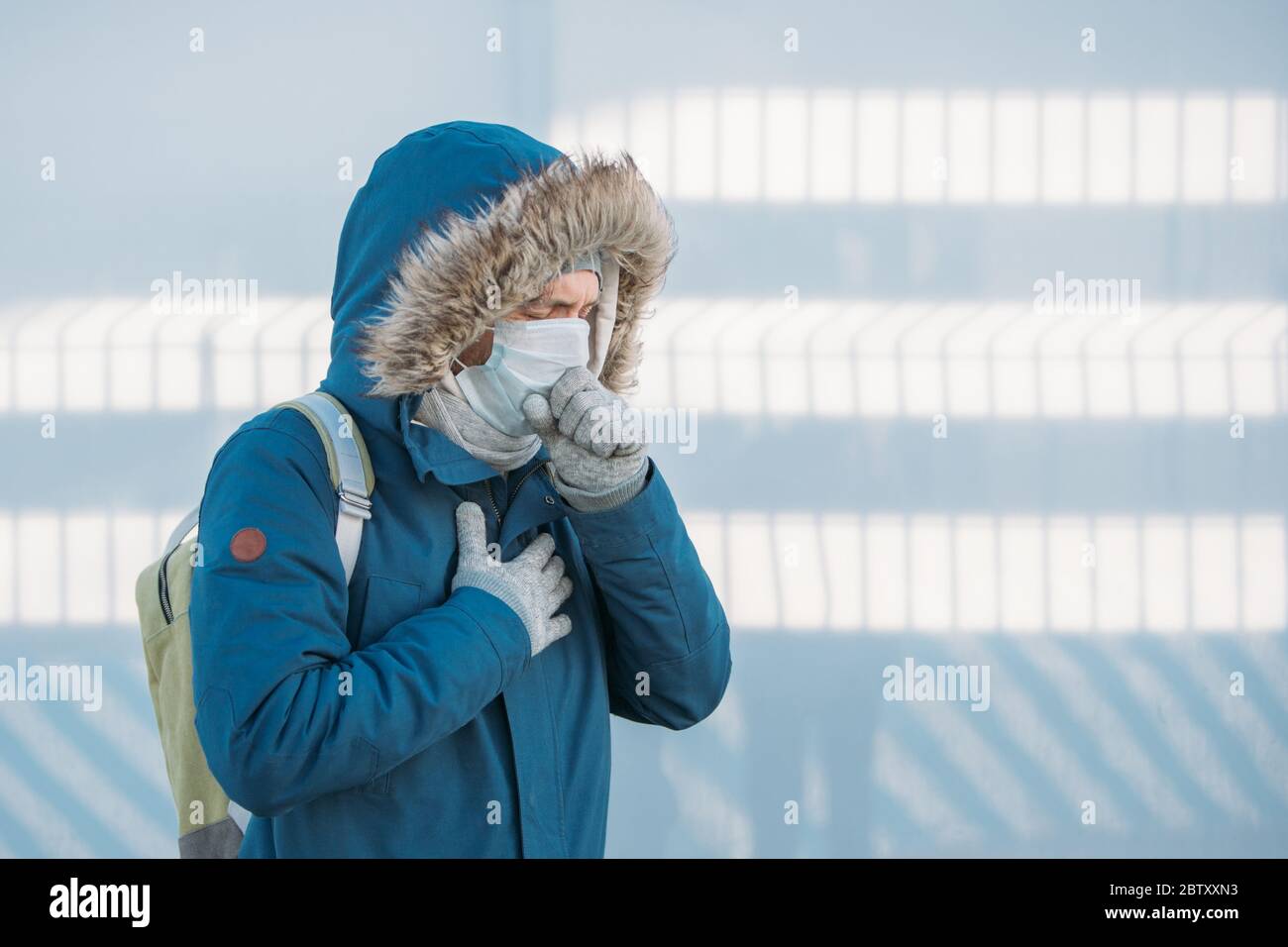 Porträt des kranken jungen Mannes in blauer Jacke auf eine Kapuze, mit einer Kälte, Gefühl, unwohl, husten, tragen medizinische Gesichtsmaske, im Freien. Krankheit, Upcomi Stockfoto