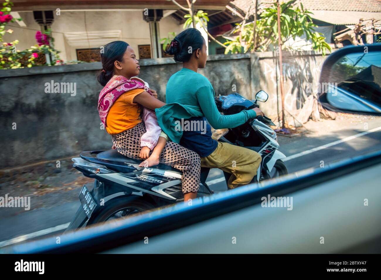 BALI, INDONESIEN - 01. Dezember 2019: Einige Leute mit Kind auf einem Roller. Balinesischer Verkehr. Traditionelles Balinesisches Stammdorf. Stockfoto