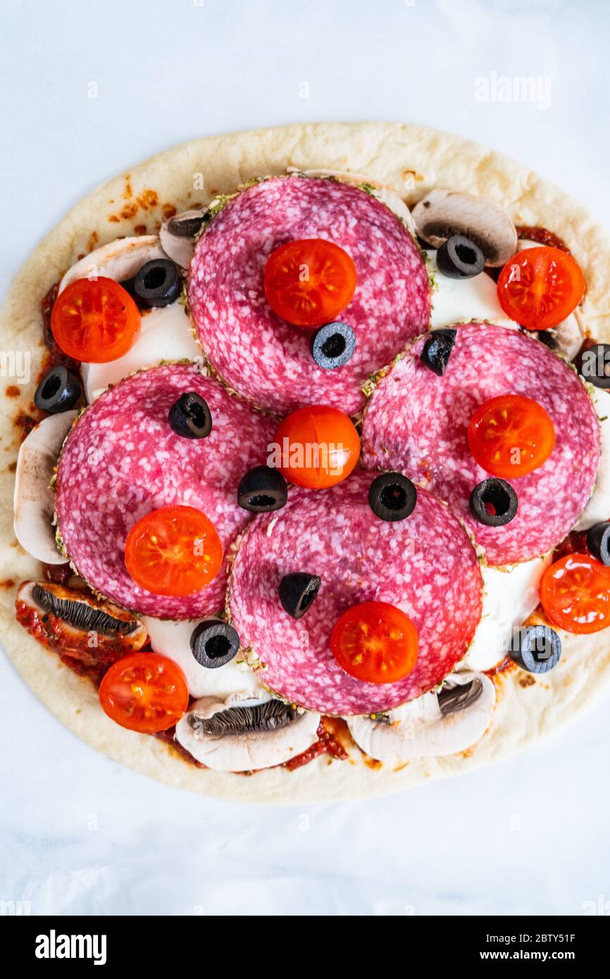 Ungebackene Pizza mit Salami, Champignon, Oliven und Kirschtomaten Stockfoto