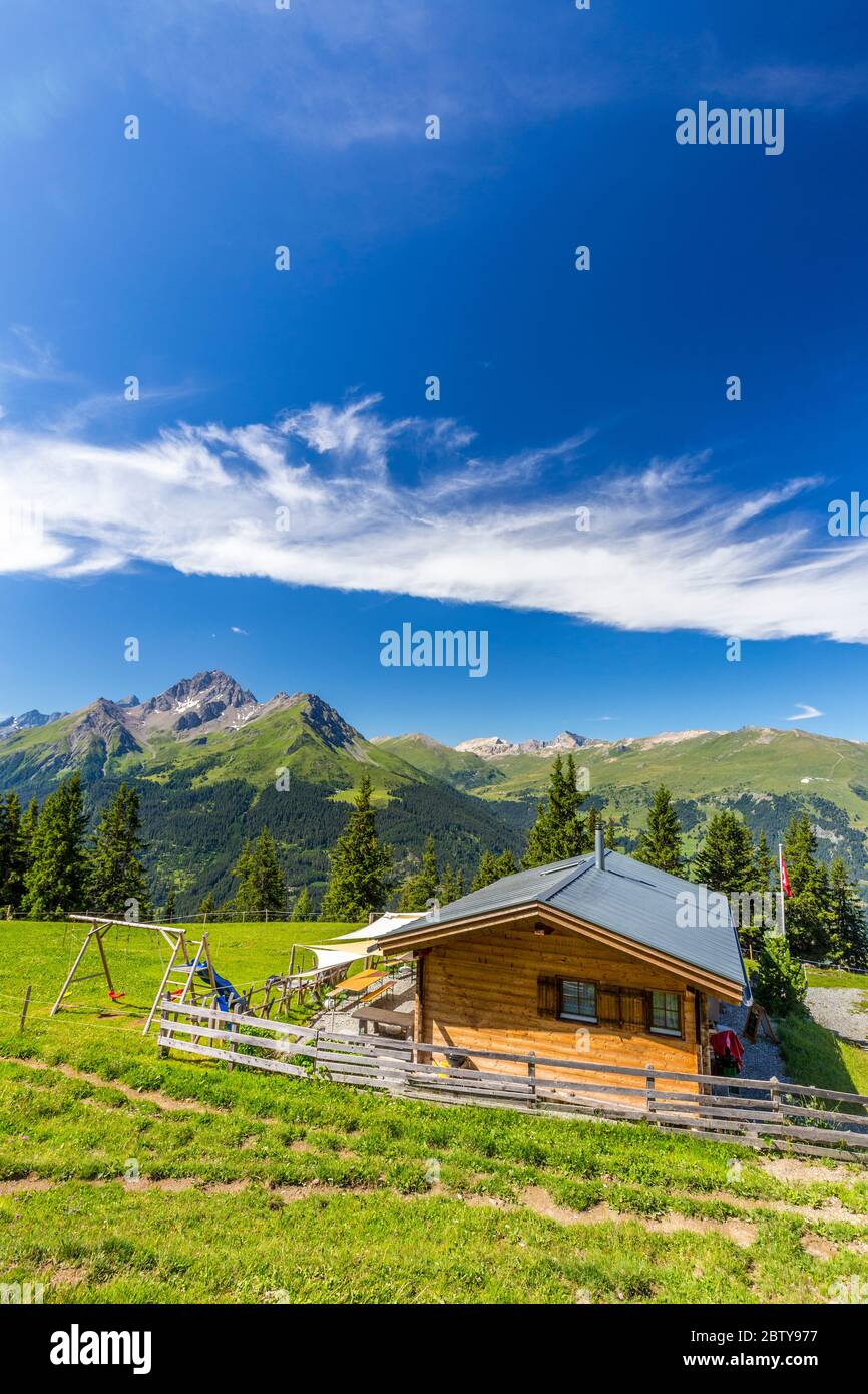Almhütte mit Schweizer Flagge, unter atemberaubenden Wolken. Surses, Surselva, Graubünden, Schweiz, Europa Stockfoto