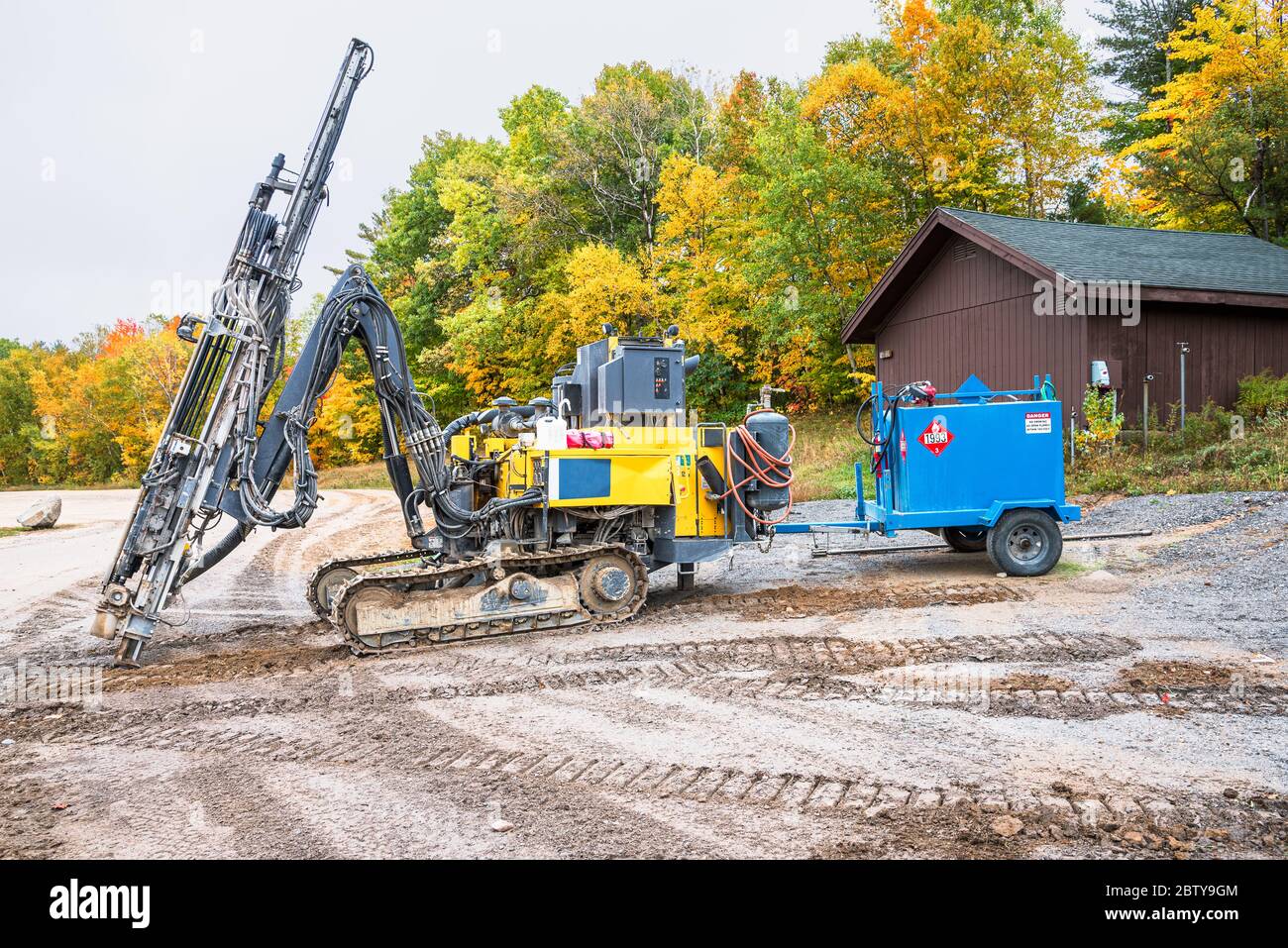 Schwere Erdbohrmaschine auf einer Baustelle mit Bäumen im Hintergrund an einem bewölkten Herbsttag Stockfoto