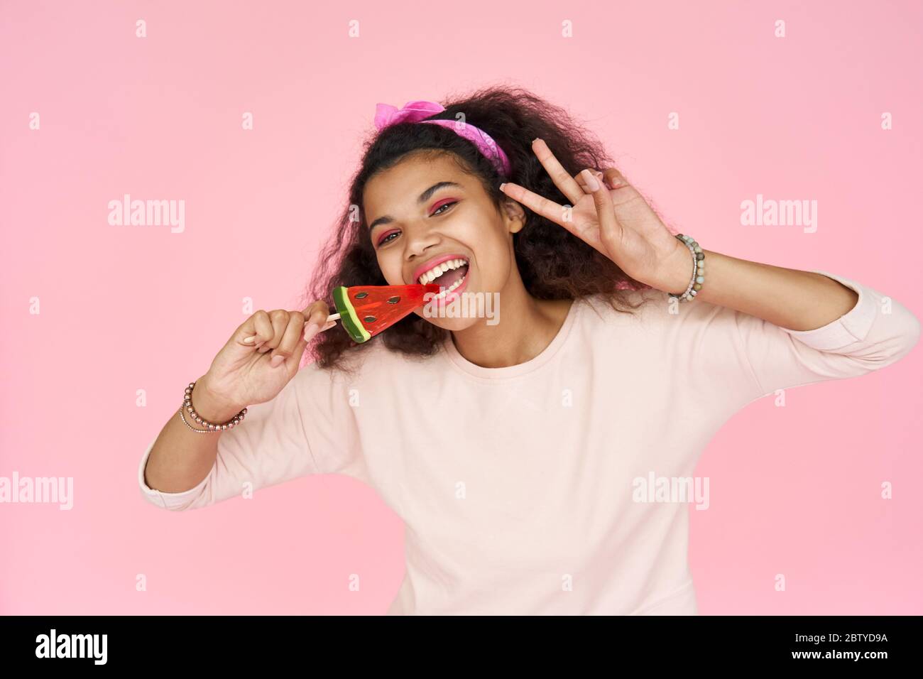 Lächelnd african gen z teen Mädchen beißen Süßigkeiten isoliert auf rosa Studio Hintergrund. Stockfoto