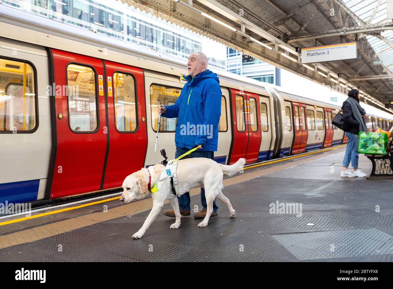 Sehbehinderte Menschen, die mit ihrem Guide Dog an der Hammersmith Station spazieren Stockfoto