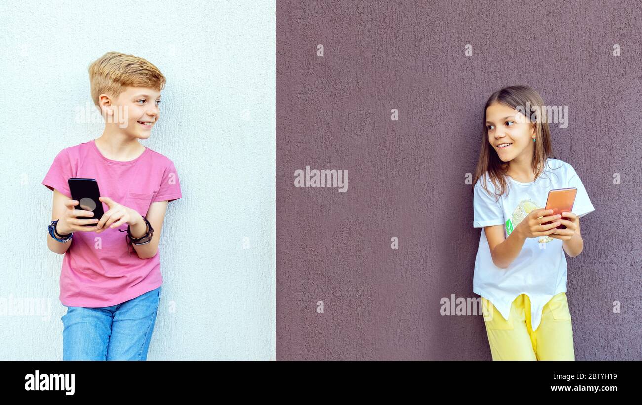Trendige Kinder, die Mobiltelefone benutzen und gleichzeitig soziale Distanz bewahren Stockfoto