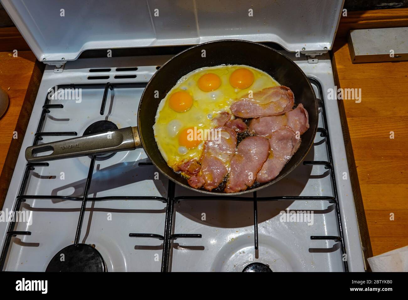 Englisches Frühstück, eine Bratpfanne auf Gasherd mit Speck und Eiern, die gebraten wurden Stockfoto