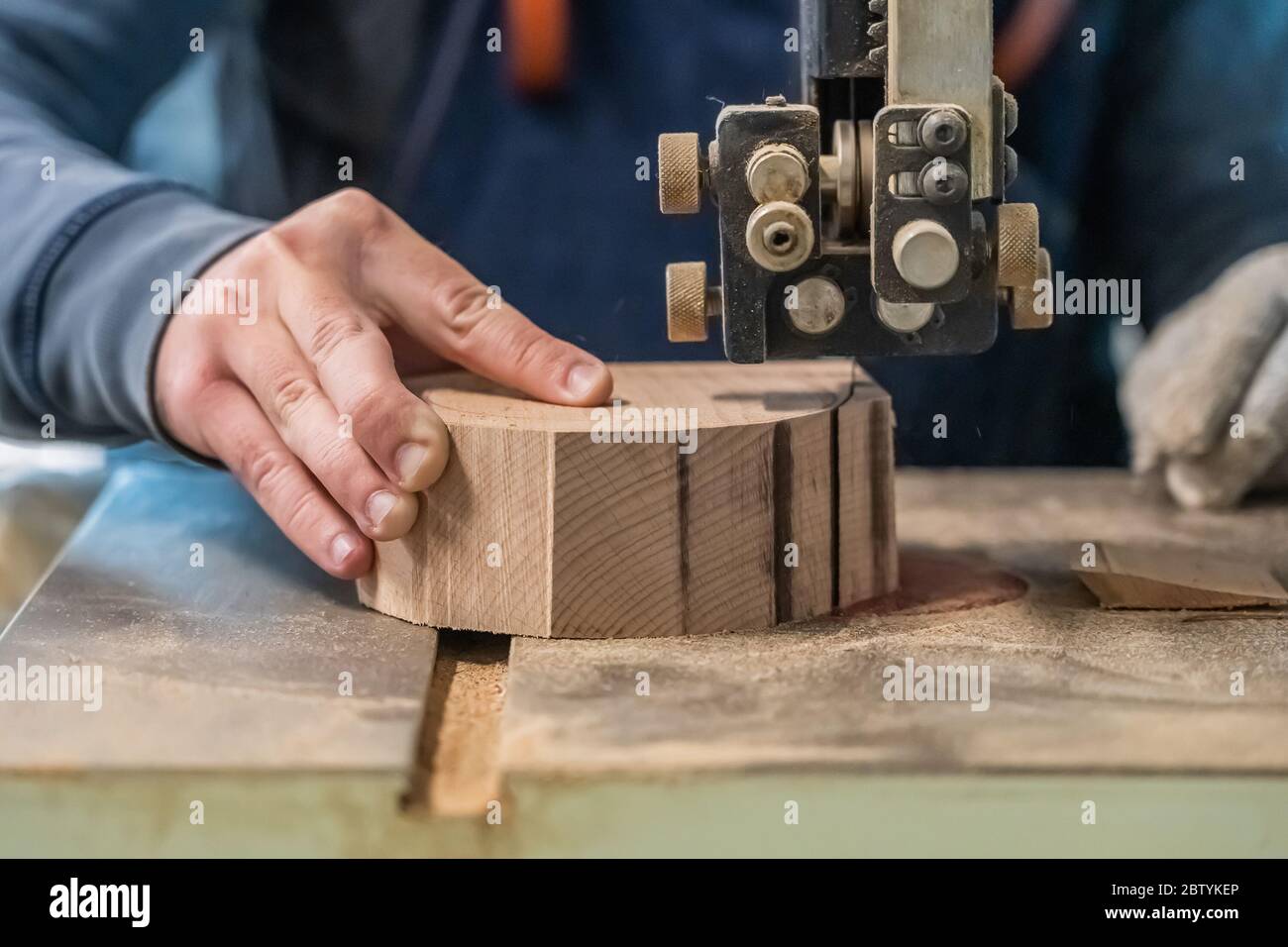 Der Zimmermann schneidet das Holzstück mit der Ausrüstung auf dem Stand. Die Hand des Mannes macht ein rundes Detail aus dem Log. Tischler verwendet elektrische Säge t Stockfoto