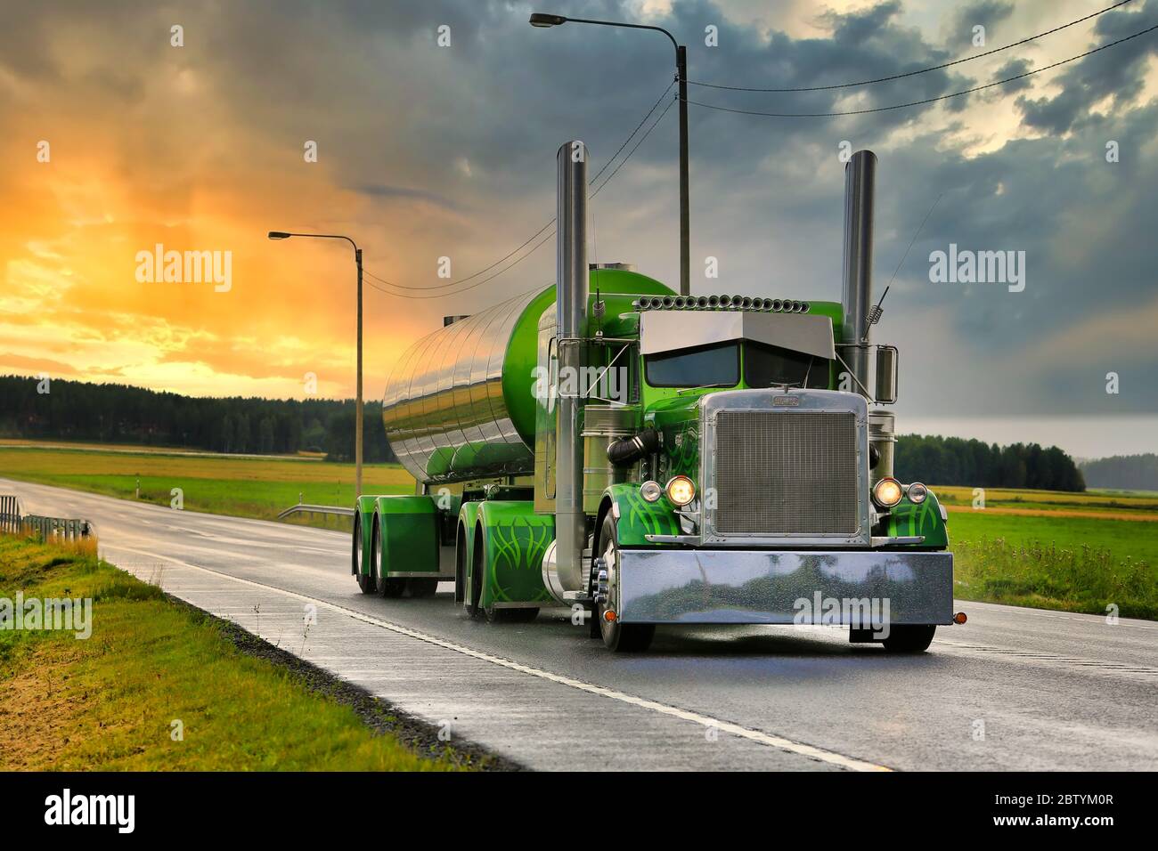 Der grüne Peterbilt 359 Tankwagen des Jahres 1971 von Fredrik Biehl fährt nach Regen auf der nassen Autobahn mit dramatischem Sonnenaufgangshimmel. SKY-Ersatz. Stockfoto