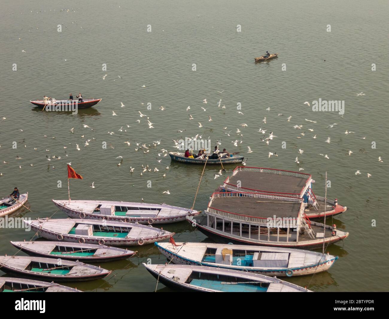 Varanasi, Uttar Pradesh, Indien - Februar 2015: Eine Luftaufnahme von hölzernen Ruderbooten auf dem Fluss Ganga mit Vögeln, die über ihnen fliegen. Stockfoto