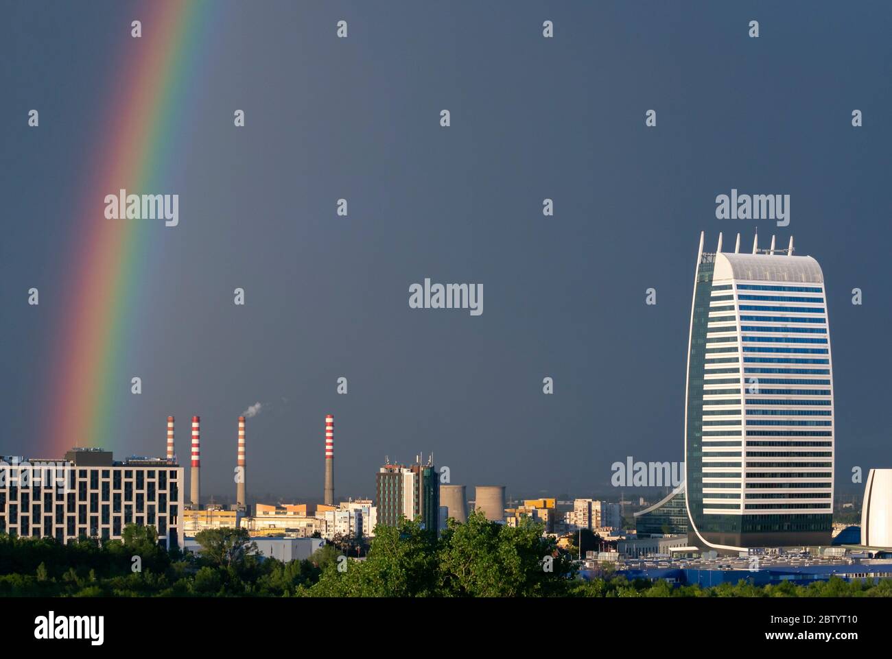 Dramatische, lebendige Stadtansicht des dunklen Himmels und des hellen Regenbogens nach dem Sturm über dem Industriekomplex in urbaner Umgebung. Stockfoto