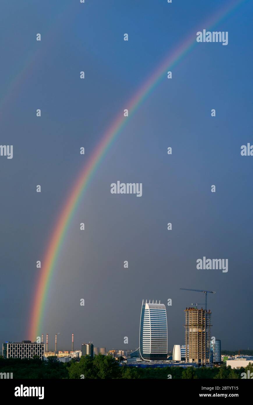 Dramatische, lebendige Stadtansicht des dunklen Himmels und des hellen Regenbogens nach dem Sturm über dem Industriekomplex in urbaner Umgebung. Stockfoto