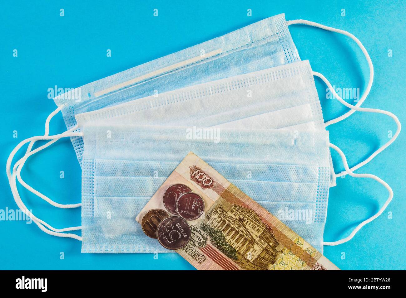 Drei medizinische Masken und russisches Geld, Banknote von 100 Rubel und Münzen auf blauem Hintergrund. Konzept des Wachstumspreises der Gesichtsmaske. Draufsicht Stockfoto