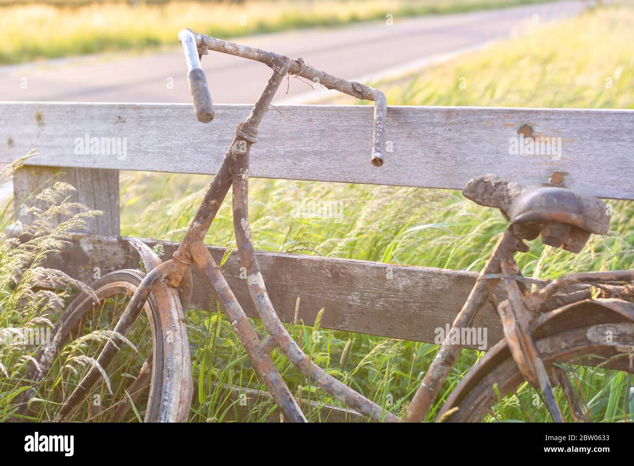 Ein altes verlassene rostige Fahrrad parkte gegen einen Holzzaun. Altmodische klassische Fahrrad steht vergessen entlang eines Radweges. Stockfoto