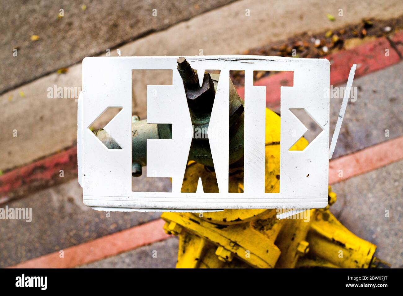 Weißes Ausgangsschild am Hydranten auf dem Bürgersteig. Abstraktes Bild des gebrochenen Exit-Schilds in einem horizontalen Farbfoto. Stockfoto