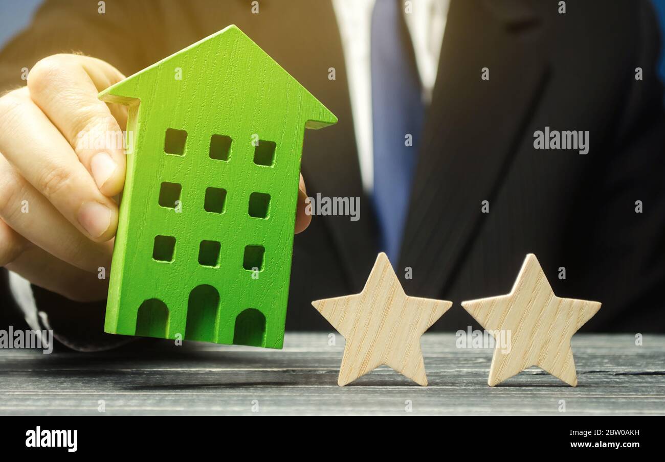 Mann hält ein Holzhaus in der Nähe von zwei Sternen. Zwei Sterne Hotel oder Restaurant. Rezension des Kritikers. Qualität und Servicelevel. Bewertung von Häusern und Privathäusern Stockfoto