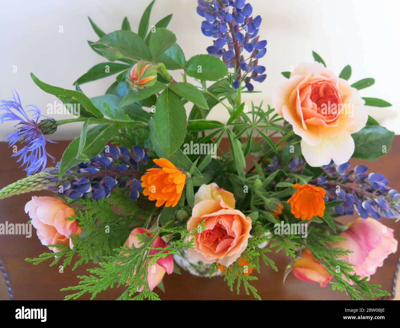 Lila, Orange und Aprikosen Schnittblumen, darunter Lupinen und Rosen, in floraler Anordnung auf einem Hallentisch. Stockfoto