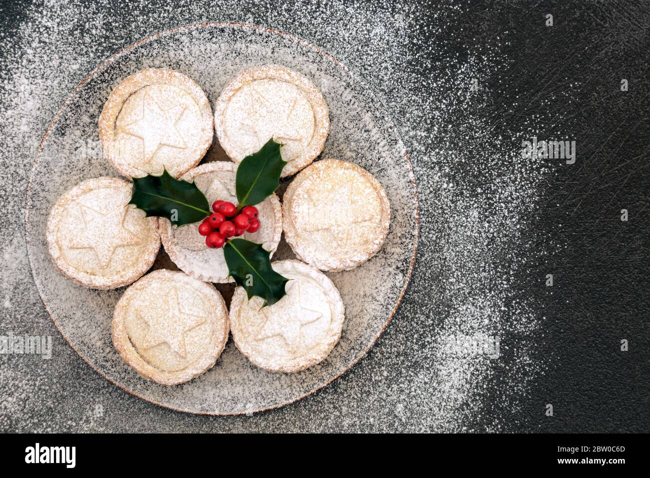 Hausgemachte Weihnachts-Hackkuchen auf einem Teller mit Winter-Beeren-Stolly & Puderzucker-Stäuben auf grauem Grunge Hintergrund. Festliche Speisenzusammenstellung. Flaches Lay, Stockfoto