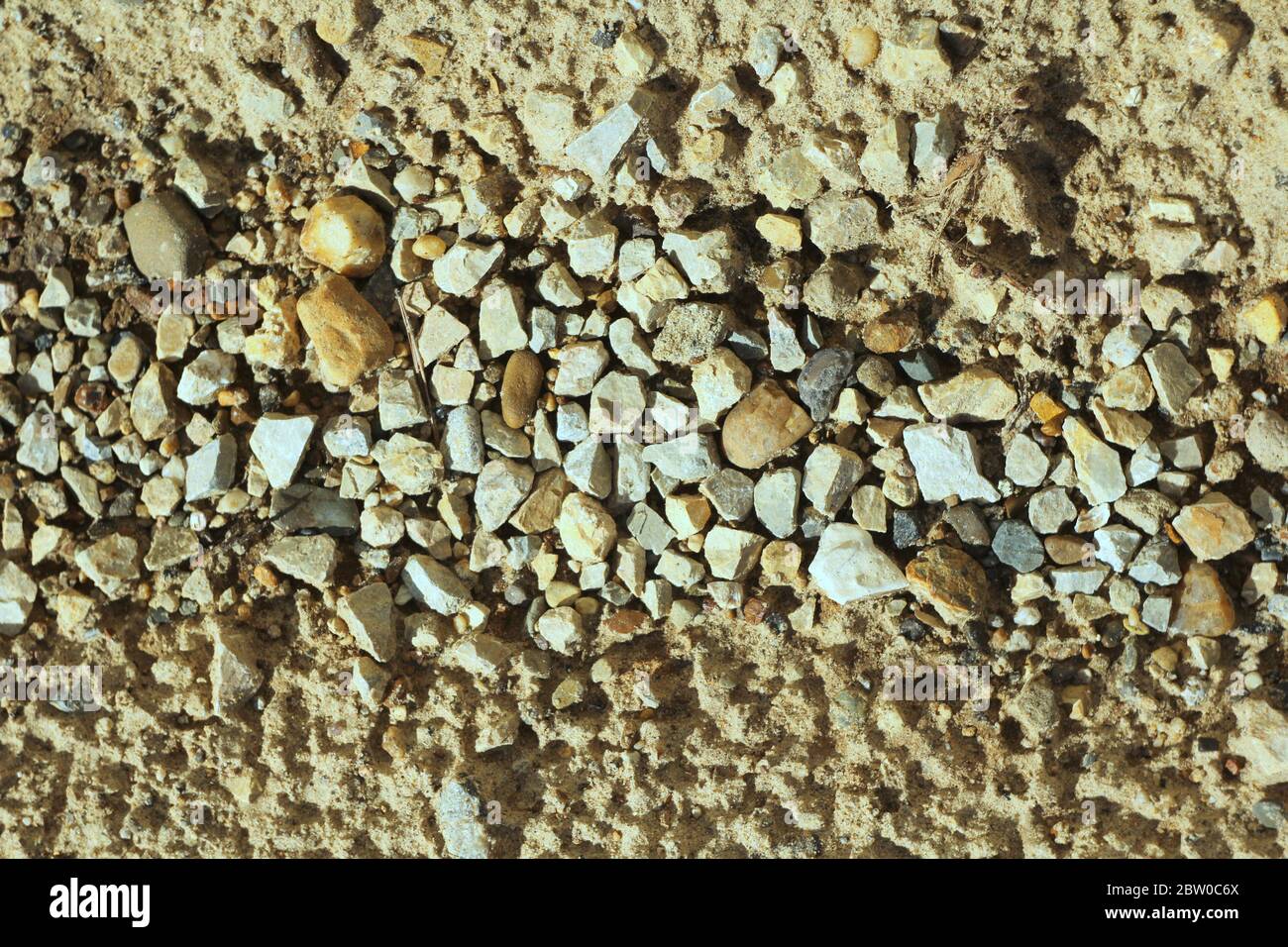 Kleine Steine auf dem Sand. Das Ufer des Stausees von Kieselsteinen, Schutt. Meer felsiger Strand. Die Textur von Stein und Sand. Der Hintergrund für das Design und der Ort für den Text. Stockfoto