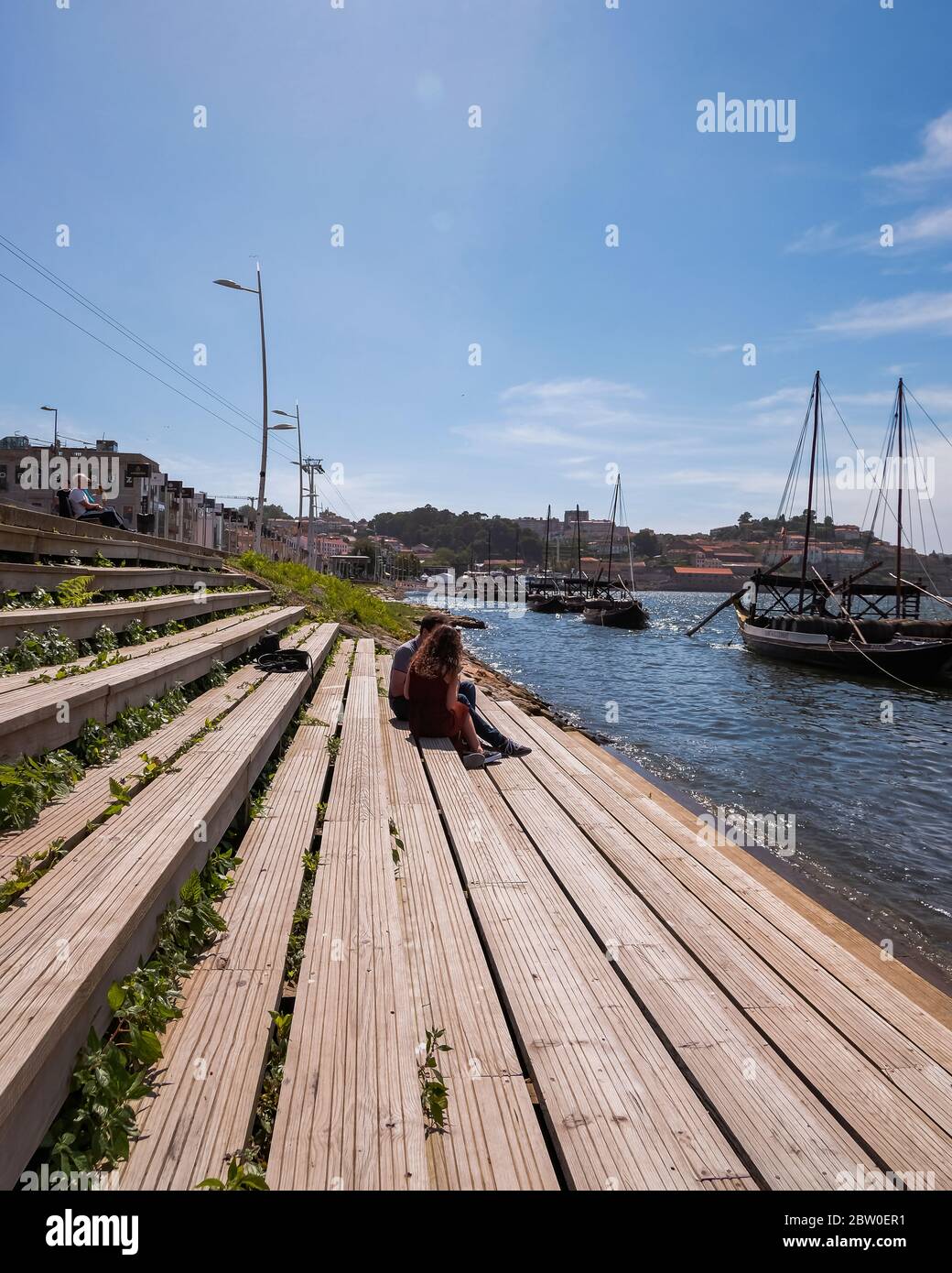 PORTO, PORTUGAL - 24. MAI 2020: Ein junges Paar auf Holztreppen am Douro Fluss mit traditionellen Rabelo Booten an einem schönen Sommertag Stockfoto