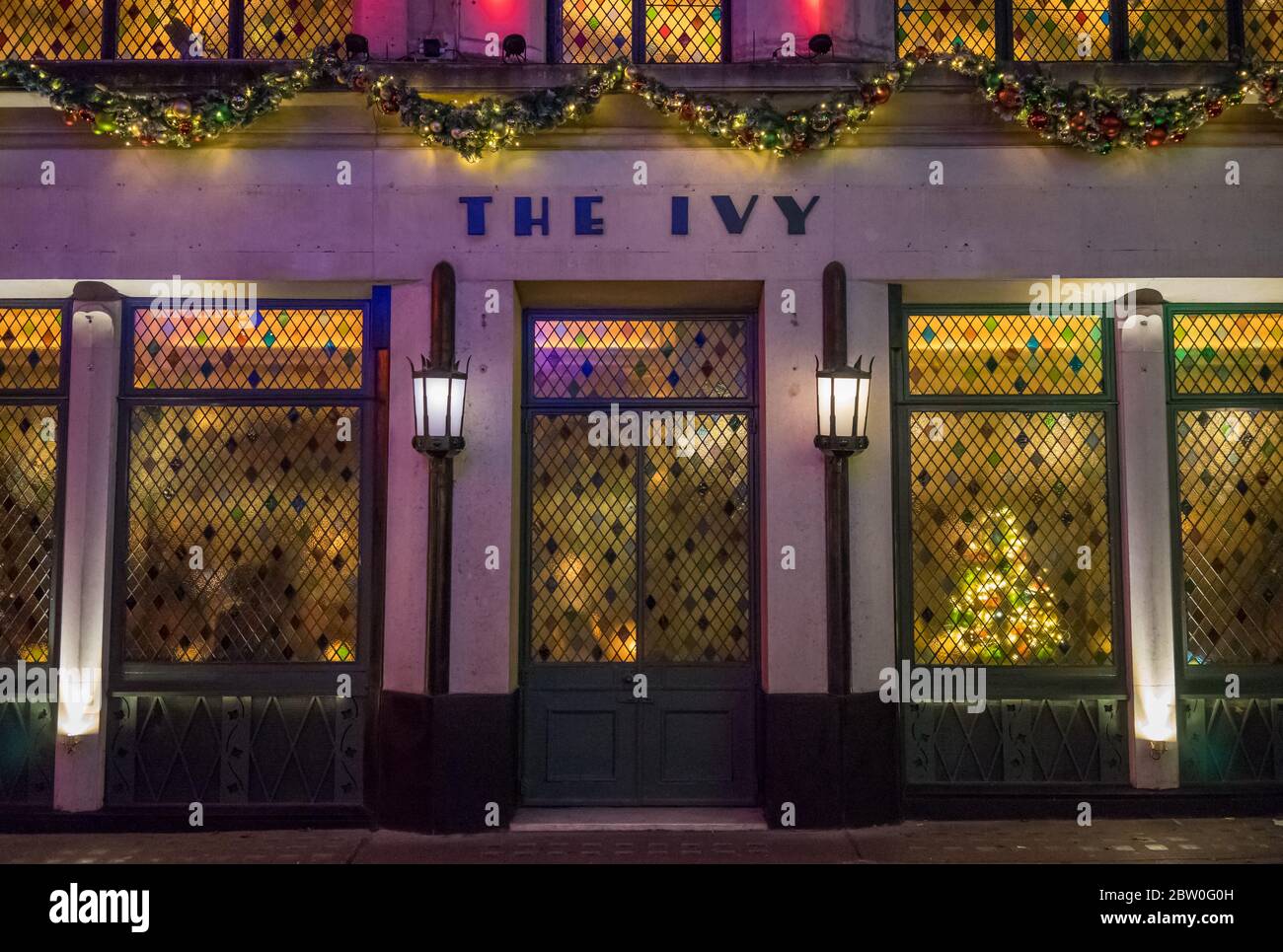 Das Ivy Restaurant am Abend mit Buntglasfenstern und Weihnachtsbeleuchtung über dem Schild. London Stockfoto