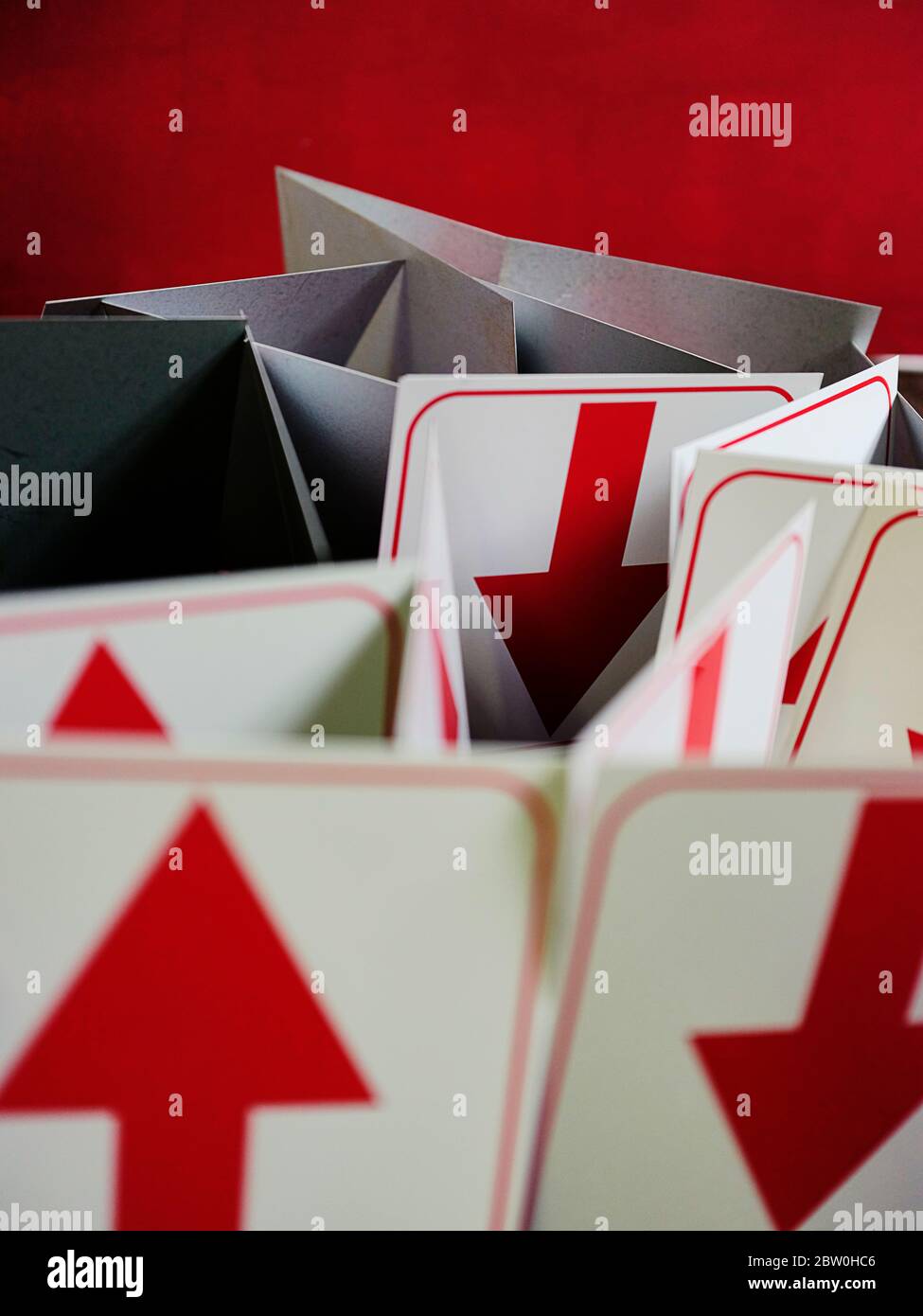 Rote Pfeile auf weißen Schildertafeln, die zufällige Richtungen vor einem roten Hintergrund mit Kopierraum anzeigen. Stockfoto