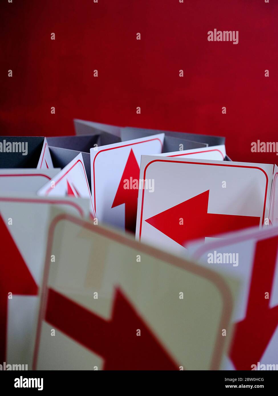 Rote Pfeile auf weißen Schildertafeln, die zufällige Richtungen vor einem roten Hintergrund mit Kopierraum anzeigen. Stockfoto