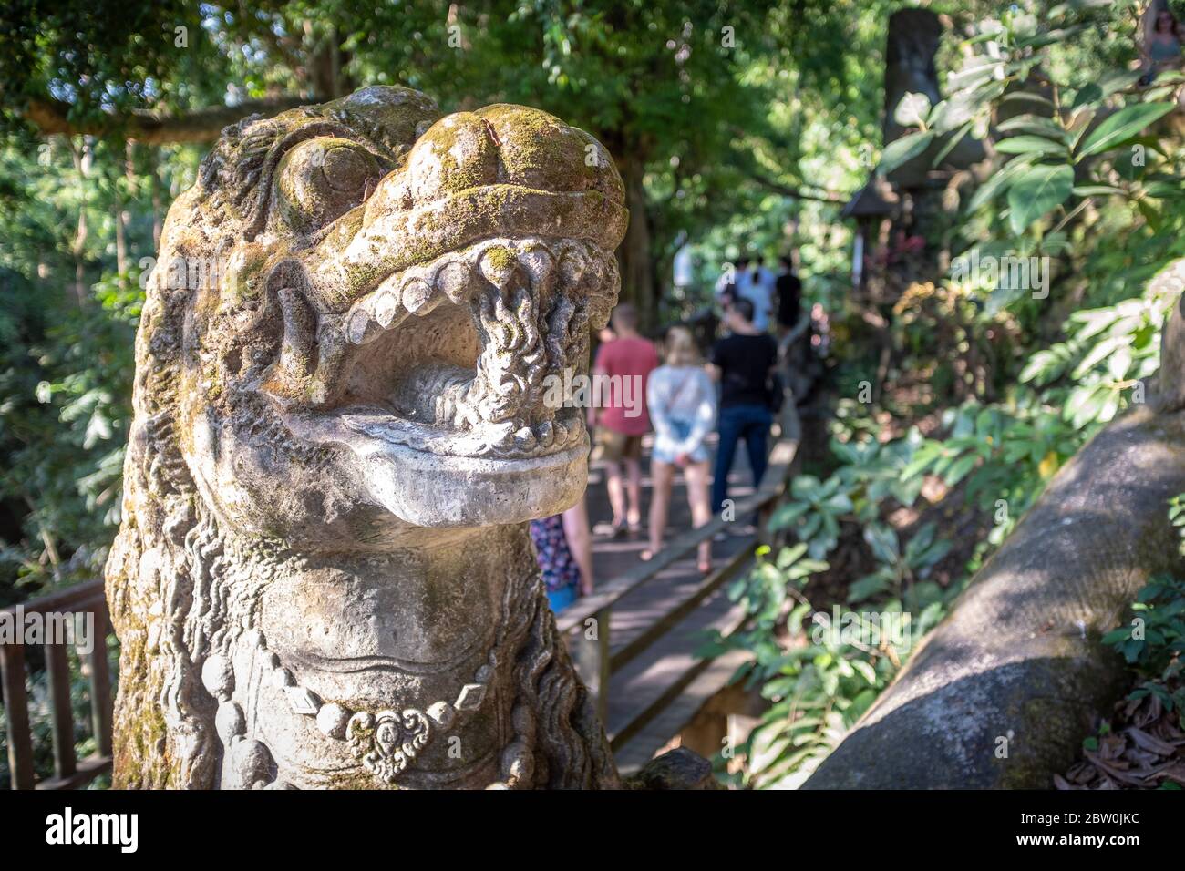 Skulptur eines Drachenkopfes und verschwommener Touristen, die im Hintergrund vorbeiziehen, im Monkey Forest Park, Ubud, Bali, Indonesien Stockfoto