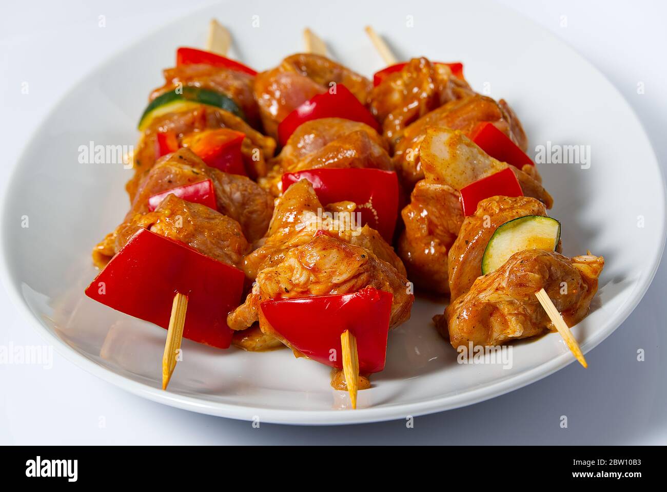 Rohes mariniertes Hühnerfleisch auf Holzspießen, Schwein, Huhn, Rindfleisch in weißem Teller auf weißem Hintergrund. Stockfoto