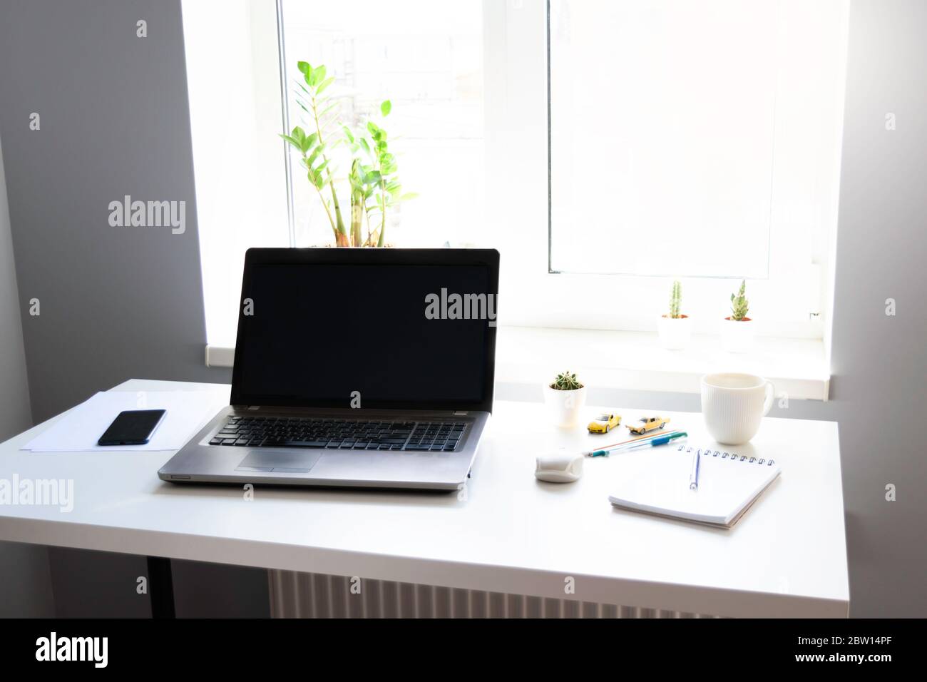 Arbeitsplatz mit Laptop mit leerem Bildschirm auf weißem Tisch mit Maus und Tasse Kaffee. Home Office und Remote-Arbeit. Stockfoto