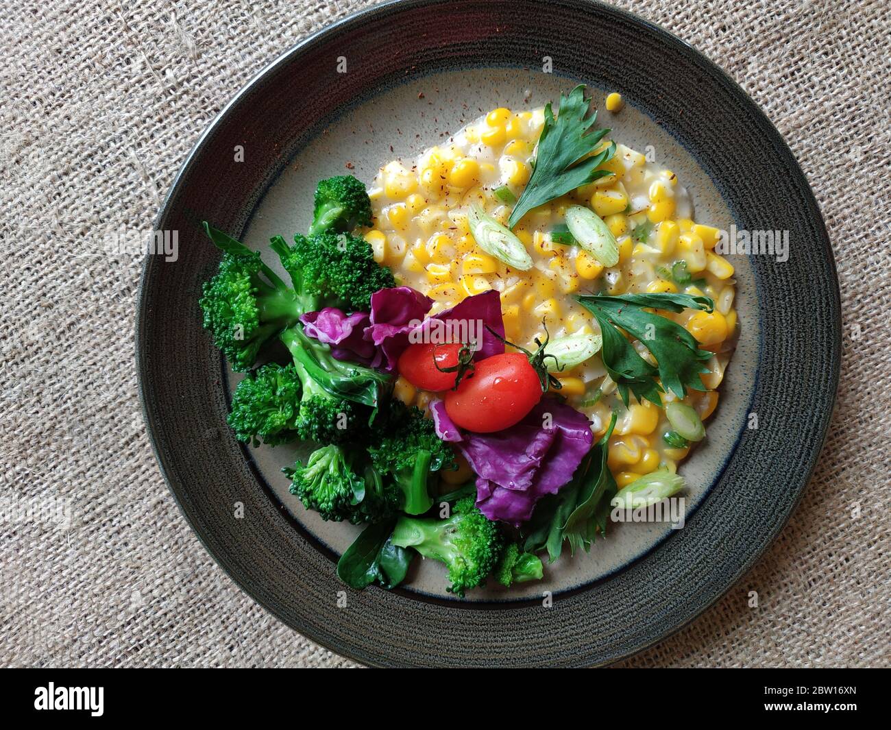 Indonesisches Maismehl mit Brokkoli, Tomaten und in Scheiben geschnittenem purple-Kohl auf dem Teller serviert Stockfoto