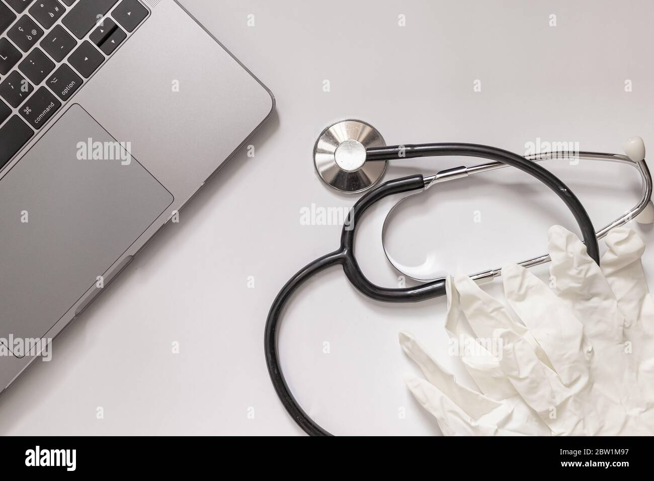 Weiße Oberfläche mit Laptop, Einweghandschuhe und Stethoskop-Luftaufnahme, Konzept von Medizin und Arzt, Kopierraum links Stockfoto