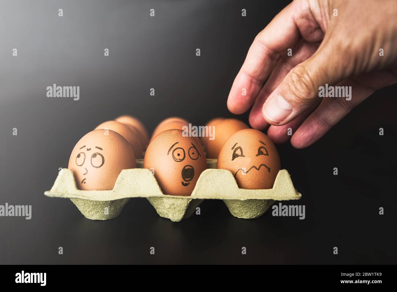 Nahaufnahme eines Dutzend Eier und eines erwachsenen Mannes Hand zu symbolisieren verschiedene Zustände von Menschen in einer Situation der Unterdrückung, erfassen, erschrecken, schleichen w Stockfoto