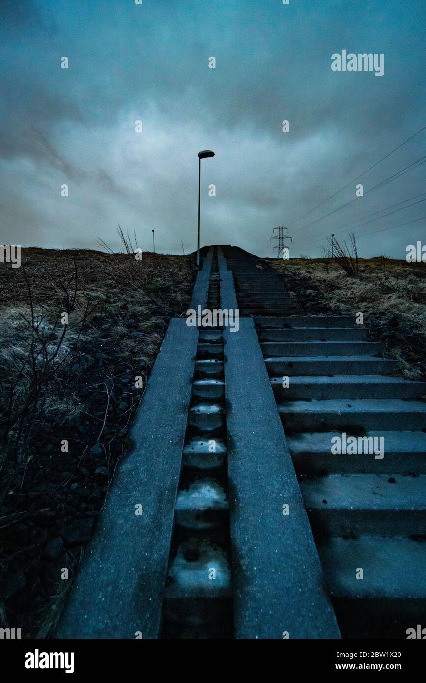 Niedriger Winkel einer alten Treppe in einem ländlichen isländischen Gebiet, der in Richtung des grauen Himmels führt Stockfoto