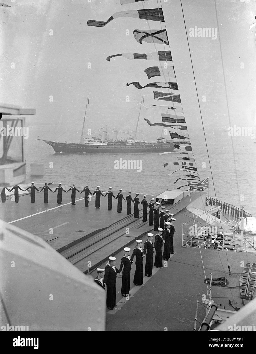 Der König bewertet Flotte bei Spithead. An Bord der königlichen Yacht, Victoria und Albert, fuhr der König durch die 5 Meilen Linie von 160 Kriegsschiffen und Handelsschiffen, als er seine Krönungsüberprüfung der britischen Marine und der Merkantile Marine in Spithead machte. Fast 300 Schiffe, darunter 17 von ausländischen Flotten, wurden überprüft. Foto zeigt, die Royal Yacht 'Victoria und Albert' vorbei an der Flugzeugträger HMS glorreichen als die Crew gekleidet Schiff. 20 Mai 1937 Stockfoto